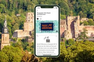 Smartphone mit Themenjahr-Tourstation vor einer Außenansicht von Schloss Heidelberg